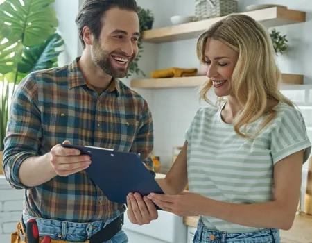 Contractor consulting a woman homeowner in a modern kitchen, smiling while reviewing renovation plans on a clipboard.